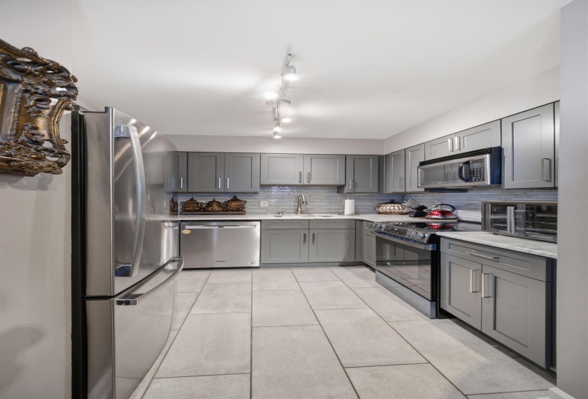 Galley kitchen featuring stainless steel appliances, gray cabinetry, track lighting, light-toned countertop, and a tiled backsplash