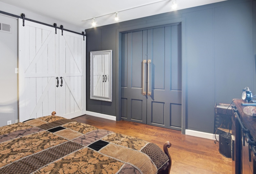 Interior space featuring wood-finish flooring, two white barn doors with black hardware, and a dark paneled wall
