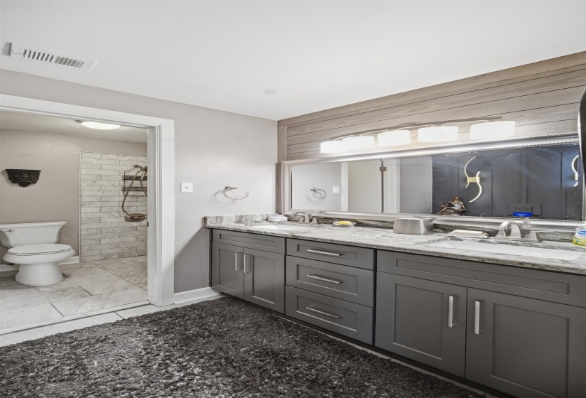Double vanity featuring gray cabinetry, chrome hardware, and a light-toned stone countertop
