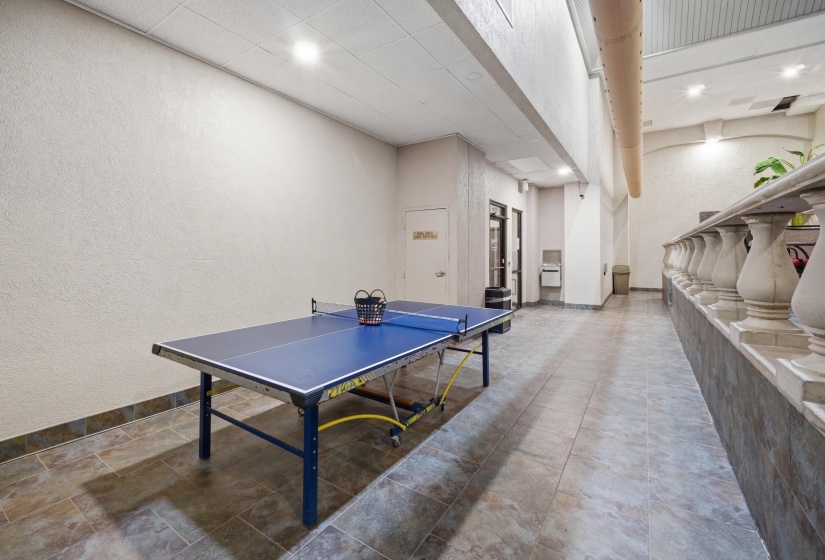Recreation room featuring a table tennis setup, tiled flooring, textured walls, recessed lighting, and a balustrade accent