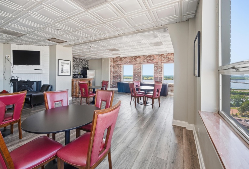Spacious common area featuring decorative tin-tile ceiling, wood-finish flooring, exposed brick accents, and multiple windows