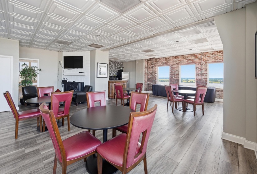 Spacious common area featuring textured ceiling, wood-finish flooring, exposed brick accent wall, and multiple windows