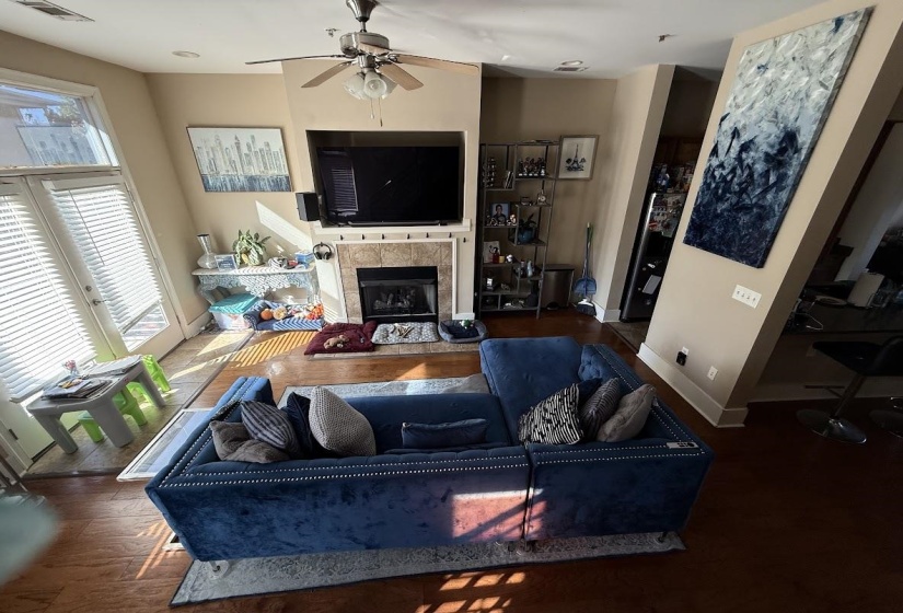 Living room with a tiled fireplace, wood finished floors, and ceiling fan