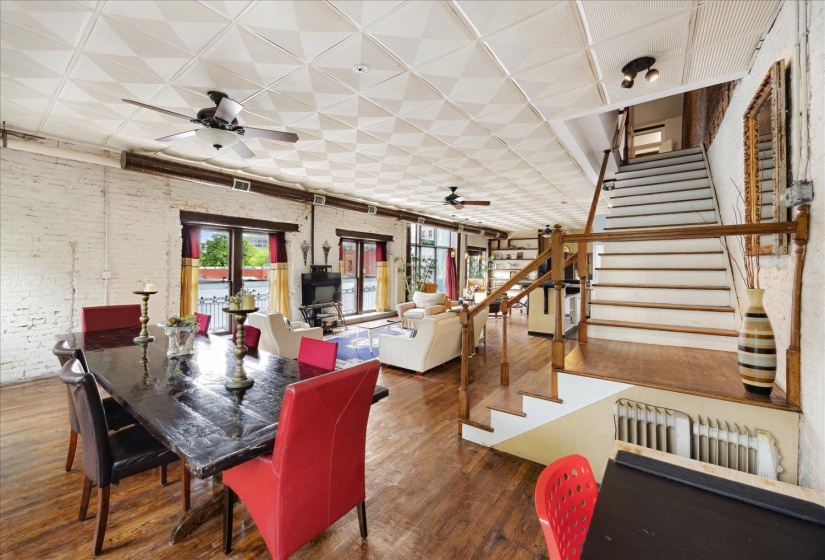 Dining room with a ceiling fan, wood finished floors, stairs, and brick wall