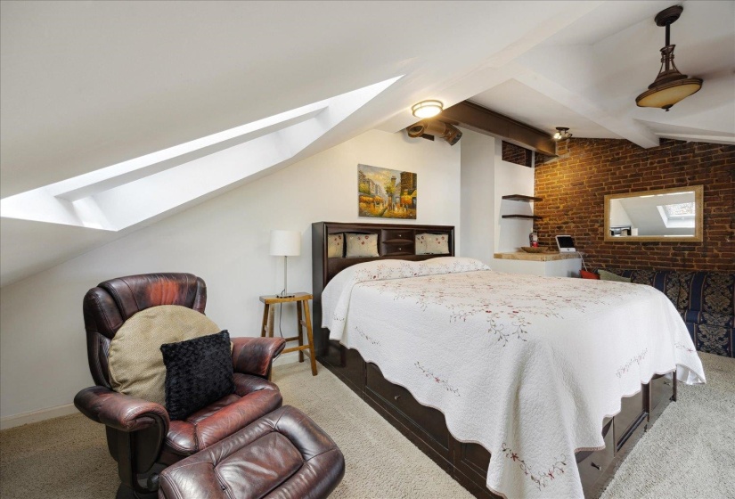 Carpeted bedroom featuring a skylight and brick wall