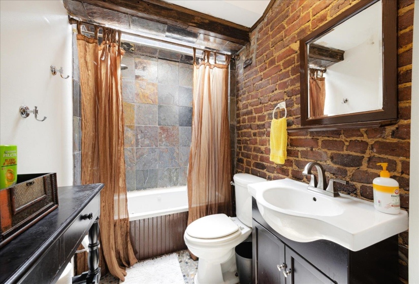 Full bathroom with vanity, toilet, shower / bath combo with shower curtain, and brick wall