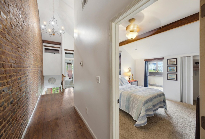 Hall featuring brick wall, beamed ceiling, a chandelier, dark wood finished floors, and baseboards
