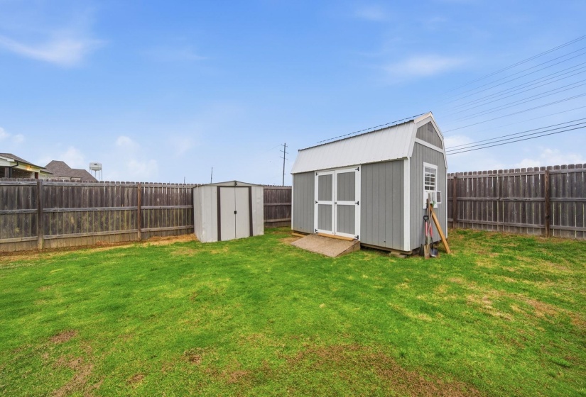 Expansive green lawn featuring a large storage shed with a gambrel roof and a smaller utility shed