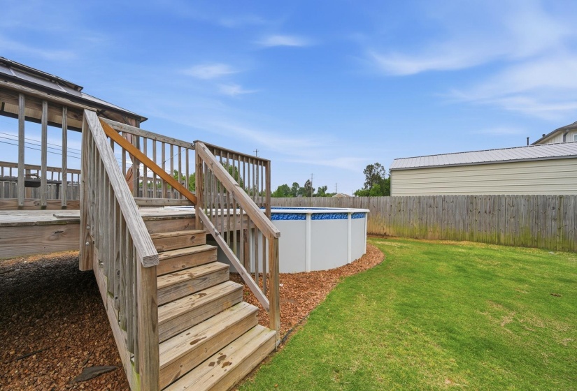 Expansive backyard featuring a wood deck with stairs, an above-ground pool, a manicured lawn, a wood fence, and a storage structure with a metal roof