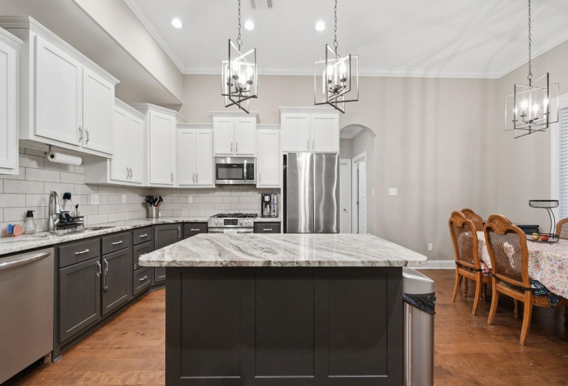 Kitchen featuring a spacious island with a natural stone countertop, two-tone cabinetry, stainless steel appliances, a subway tile backsplash, and wood-finish flooring