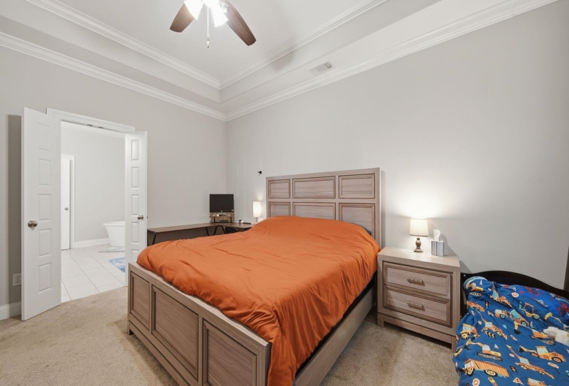 Carpeted bedroom featuring a tray ceiling, crown molding, and a ceiling fan with integrated lighting