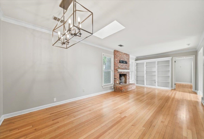Spacious room with wood-finish flooring, a brick fireplace, built-in shelving, crown molding, and a modern geometric chandelier