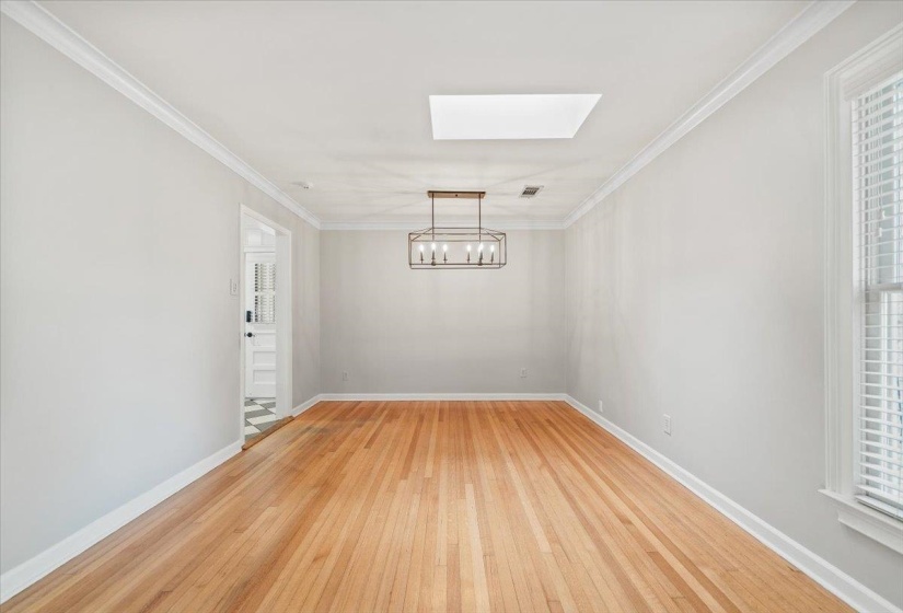 Spacious room featuring wood-finish flooring, a contemporary chandelier, a ceiling skylight, and white window blinds
