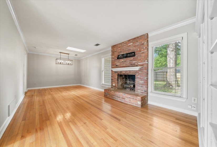 Spacious interior featuring a prominent brick fireplace with a white mantel, wood-finish flooring, white crown molding, and a modern rectangular chandelier