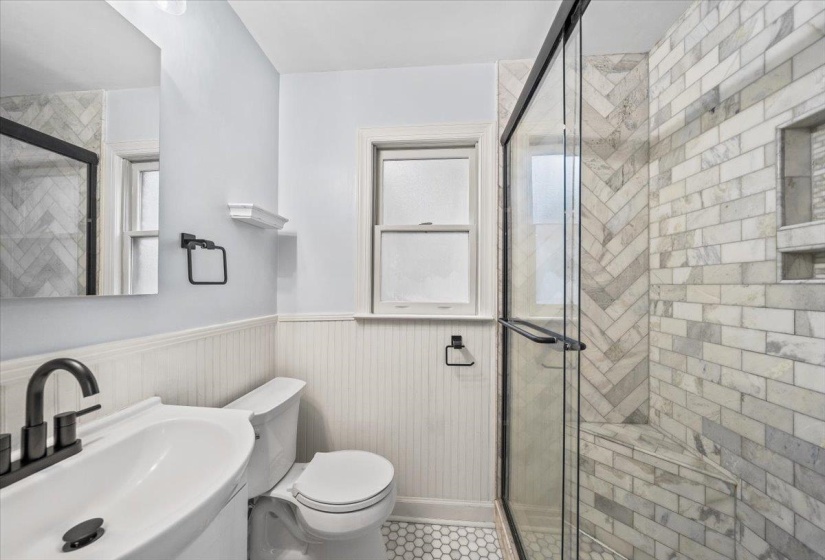 Modern bathroom featuring a walk-in shower with a glass enclosure, herringbone pattern tile, and a built-in bench