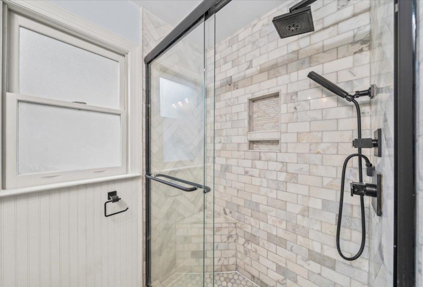Shower enclosure featuring subway tile surround, integrated shower niche, and matte black fixtures