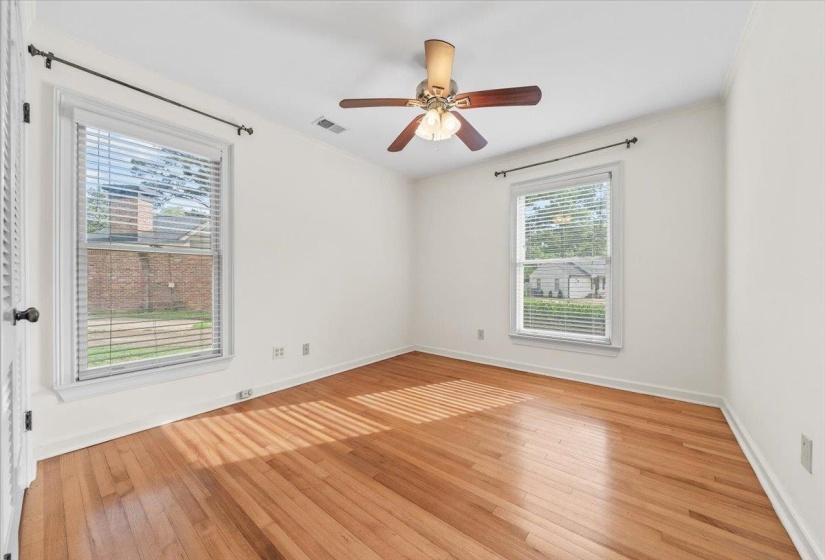Bright room featuring wood-finish flooring, two windows with blinds, a ceiling fan with light fixture, and white walls
