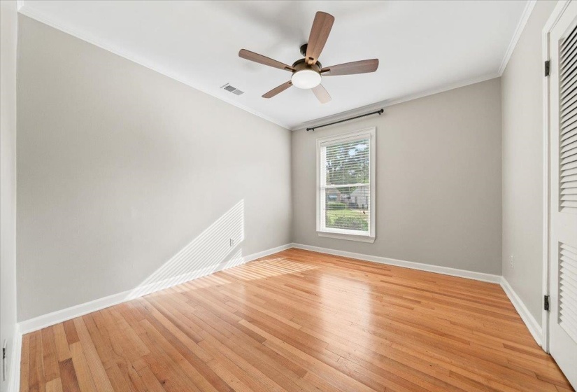 Hardwood flooring throughout featuring white baseboards, crown molding, and a central ceiling fan with integrated lighting