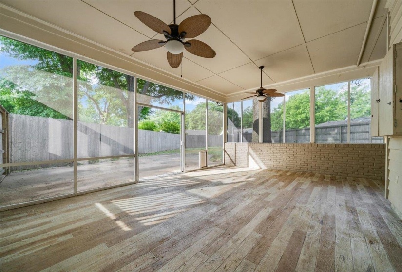 Spacious screened porch featuring wood-finish flooring, two ceiling fans, and a partial brick wall