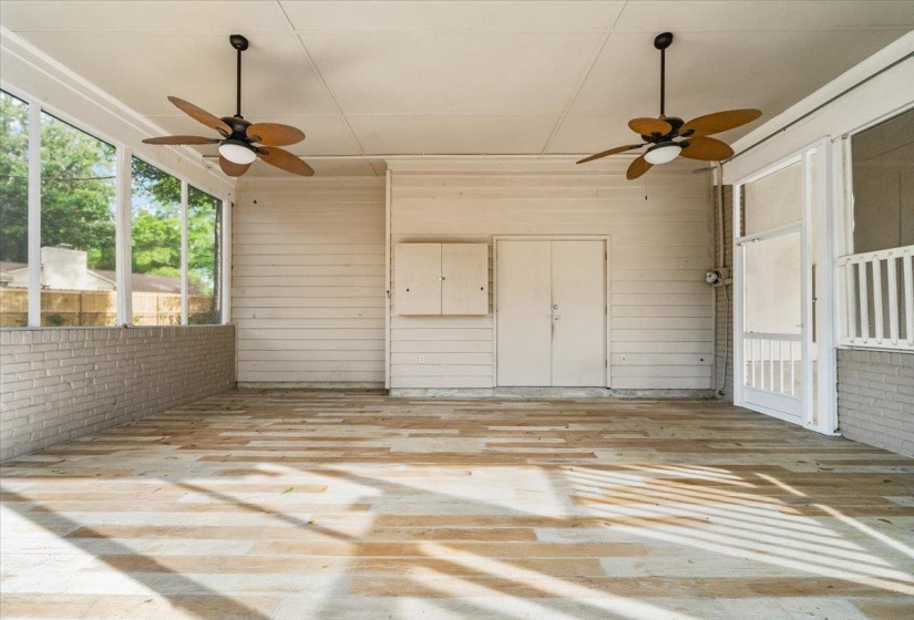 Screened porch featuring light-toned wood-finish flooring, white brick wainscoting, and two ceiling fans with integrated lighting