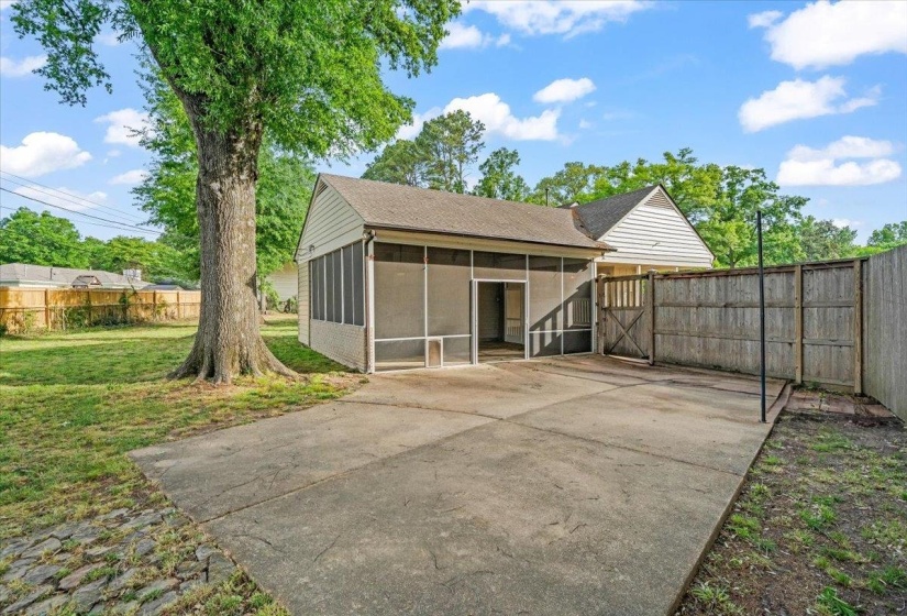 Expansive concrete patio with a screened-in porch entrance, bordered by a privacy fence and a mature tree