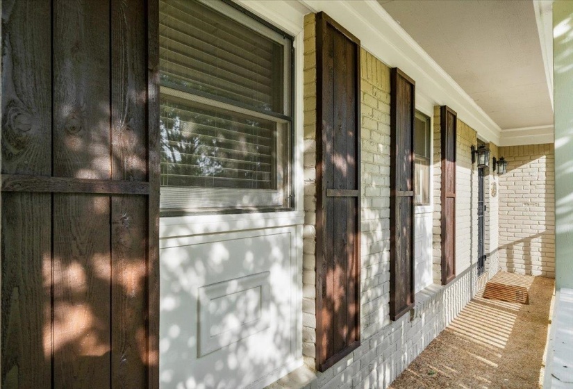 Brick exterior with decorative wood shutters, white trim, and a covered porch featuring wall-mounted sconces