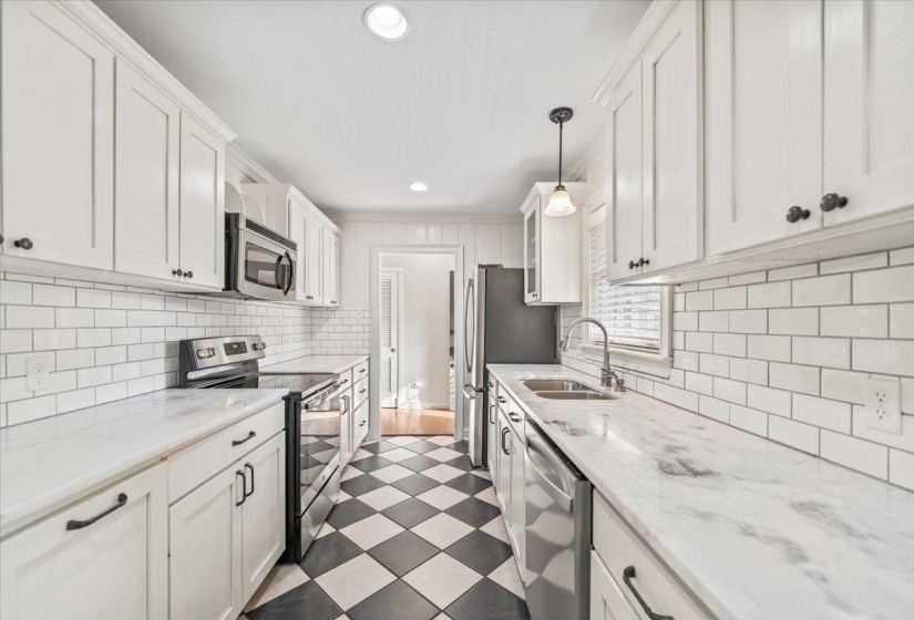 Galley kitchen featuring white shaker cabinetry, stainless steel appliances, white subway tile backsplash, and marble-finish countertops