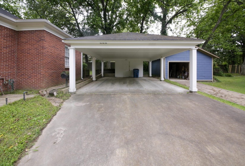 Expansive concrete driveway leading to a multi-car carport featuring white columns and a flat roofline