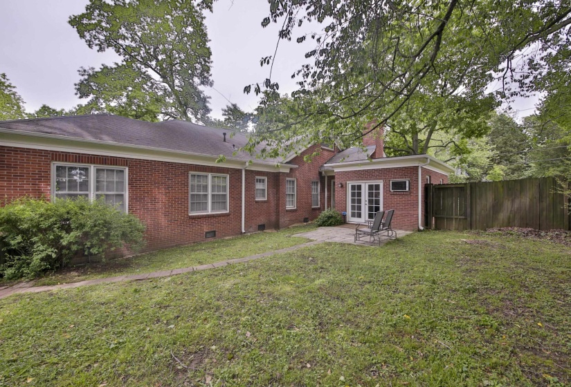 Brick exterior featuring multiple windows, a rear patio with double French doors, and mature trees providing natural canopy