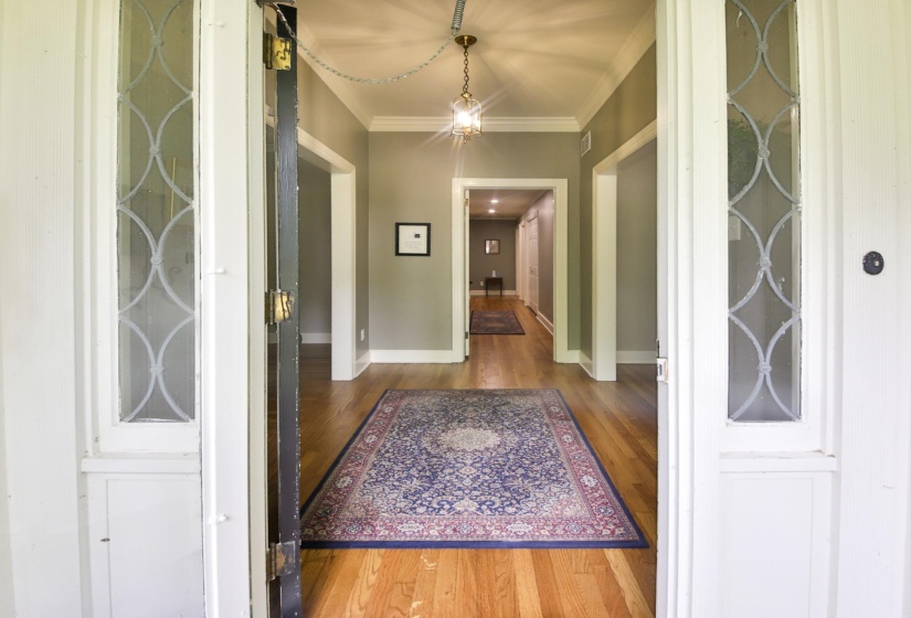 Entryway featuring hardwood flooring, crown molding, and a brass-finish pendant light fixture