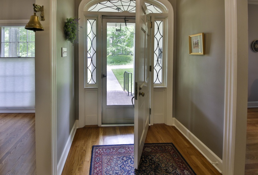 Arched front entry door with decorative glass sidelights, featuring hardwood flooring and white trim throughout