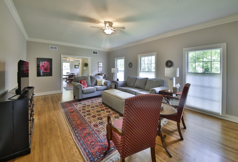 Spacious living area featuring wood-finish flooring, crown molding, and a ceiling fan with integrated lighting