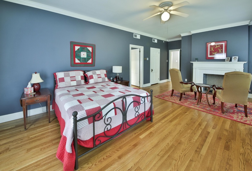 Spacious room featuring hardwood flooring, crown molding, a built-in fireplace with a white mantel, and a ceiling fan