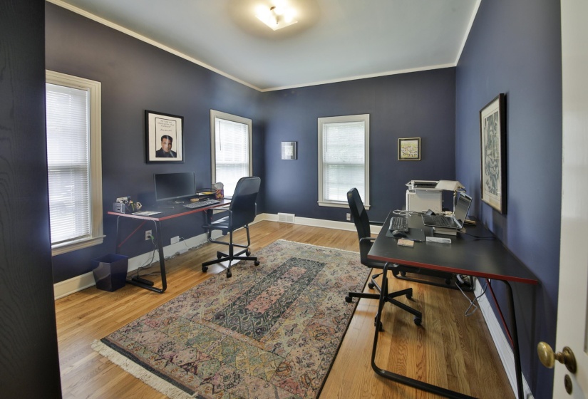 Room featuring hardwood flooring, multiple windows with blinds, a ceiling-mounted light fixture, and crown molding