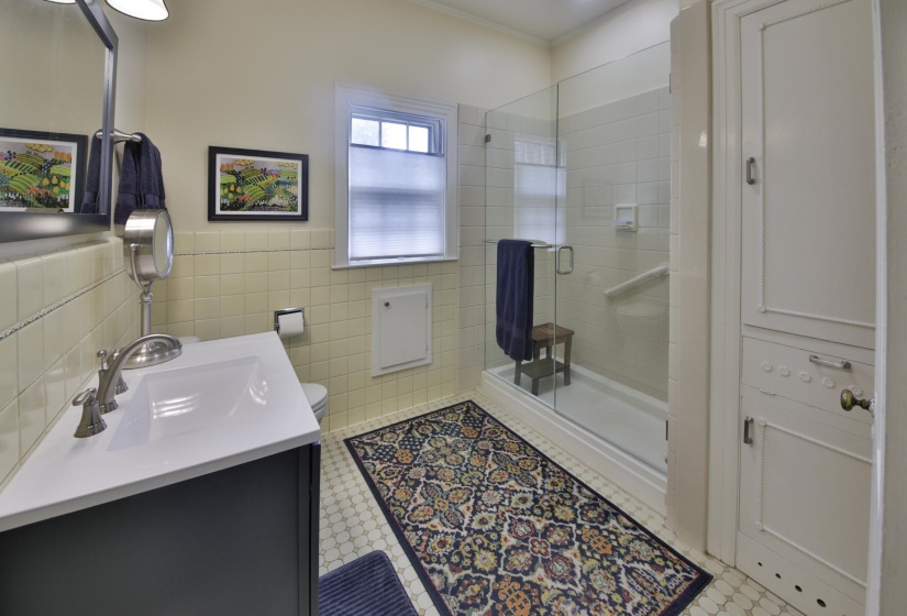 Bathroom featuring a walk-in shower with glass enclosure, white square tile flooring, a dark vanity with a white countertop and integrated sink, and an opaque window