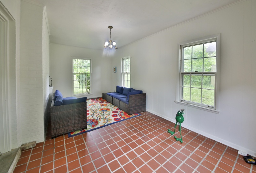 Spacious room featuring square terracotta tile flooring, white painted walls, and multiple large windows with grid patterns