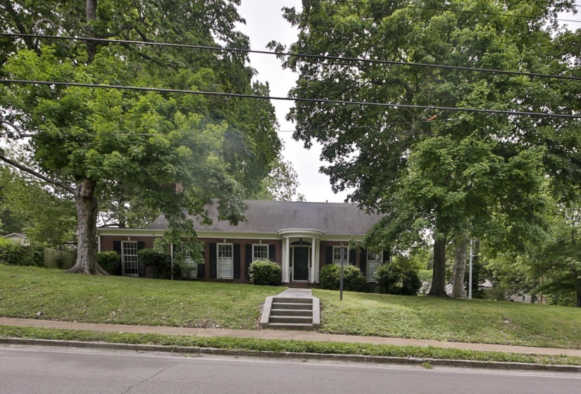 Brick exterior residence with a gently sloped lawn, mature trees, and a central entry with a curved portico