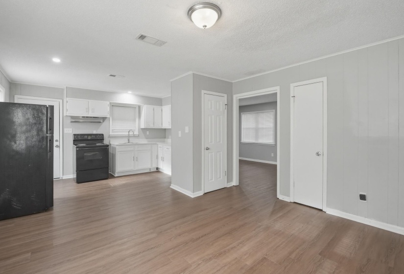 Open-concept living area with wood-finish flooring, light gray walls, white baseboards, a flush-mount ceiling light, and white paneled doors