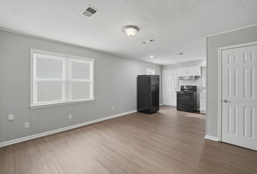 Open-concept living space with wood-finish flooring, light grey paneling, and a contemporary kitchen