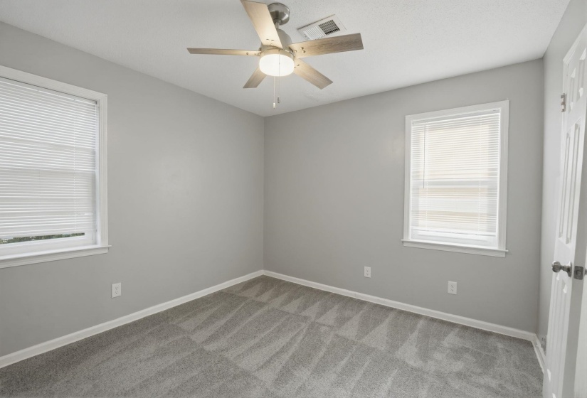 Spacious room featuring neutral gray walls, a ceiling fan with light fixture, and plush patterned carpeting