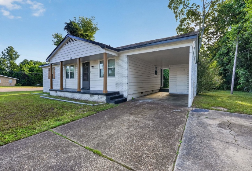 White brick and siding exterior featuring a covered front porch with wood-finish columns, a carport, a paved driveway, and a front lawn