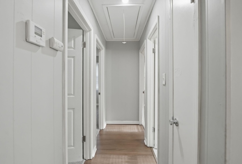Hallway featuring wood-finish flooring, white paneled walls, and multiple panel doors