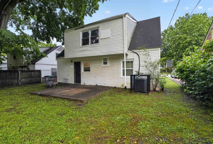 Rear exterior featuring white vinyl siding, a black shingle roof, and a concrete patio