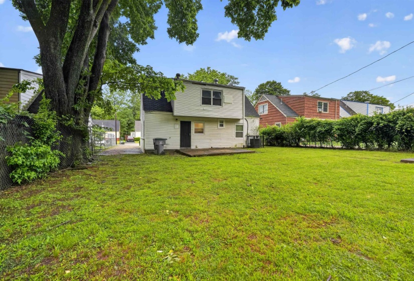 Expansive grass yard with mature trees and a chain-link fence