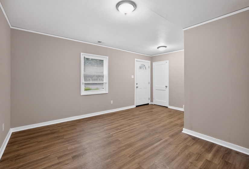 Spacious room featuring wood-finish flooring, neutral-toned walls, white trim, and a white interior door