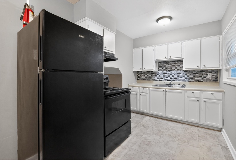 Kitchen featuring white cabinetry, light countertops, a patterned tile backsplash, and a double basin sink