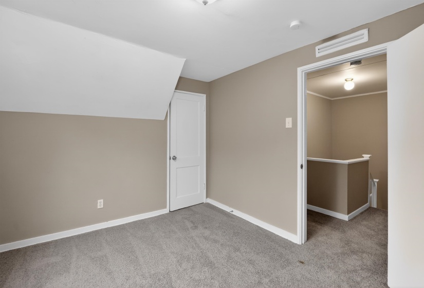 Carpeted room with sloped ceiling, painted walls, white trim, and a white paneled door
