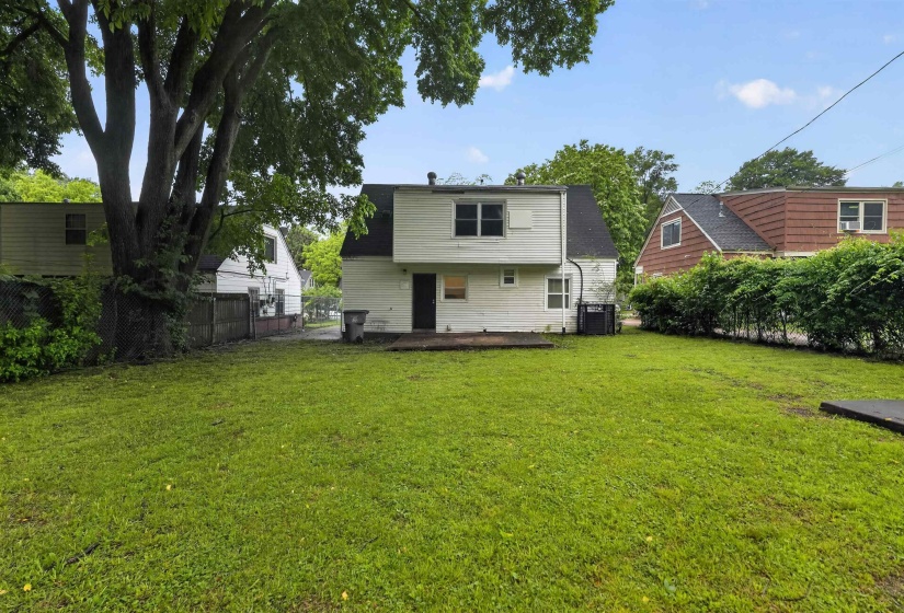 Expansive rear yard featuring green lawn, mature trees, and a concrete patio