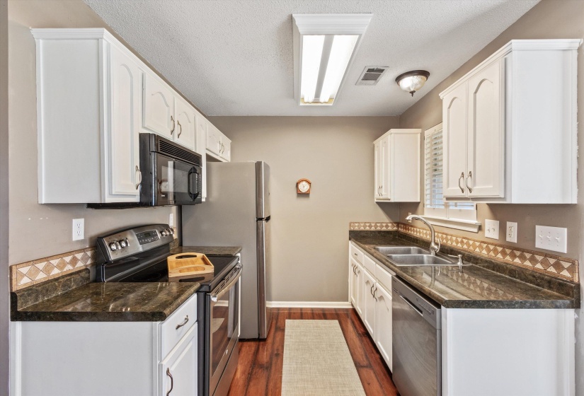 Kitchen featuring white cabinetry, dark stone countertops, and wood-finish flooring