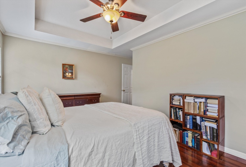 Bedroom featuring wood-finish flooring, a tray ceiling, and a ceiling fan with integrated lighting